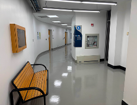 Entrance into the K Wing from the J Wing. A little corner tucked away, there are many rooms and it feels like a liminal space, no people nothing. Signs pointing towards Sheridan's Generator. A bench to sit on. Hallway is curved.